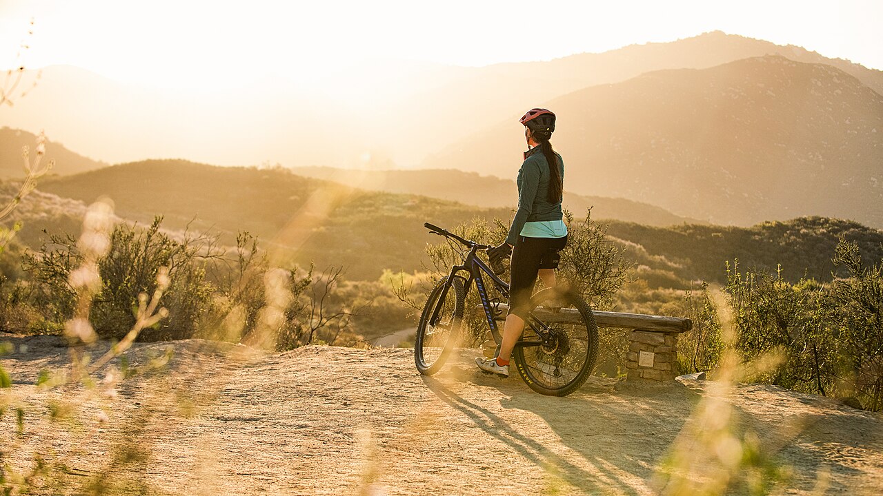 A cyclist stands with a mountain bike at a Daley Ranch overlook in golden sunrise light.
