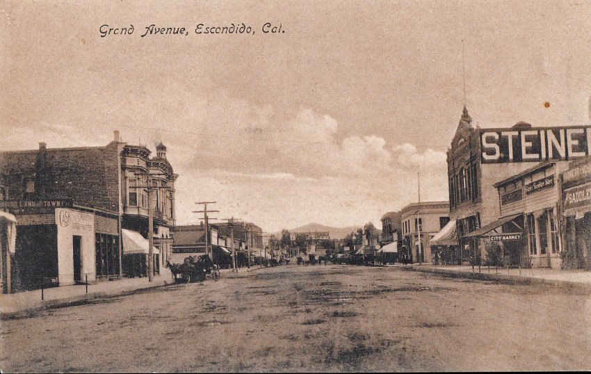 A broad unpaved Grand Avenue lined with early storefronts.