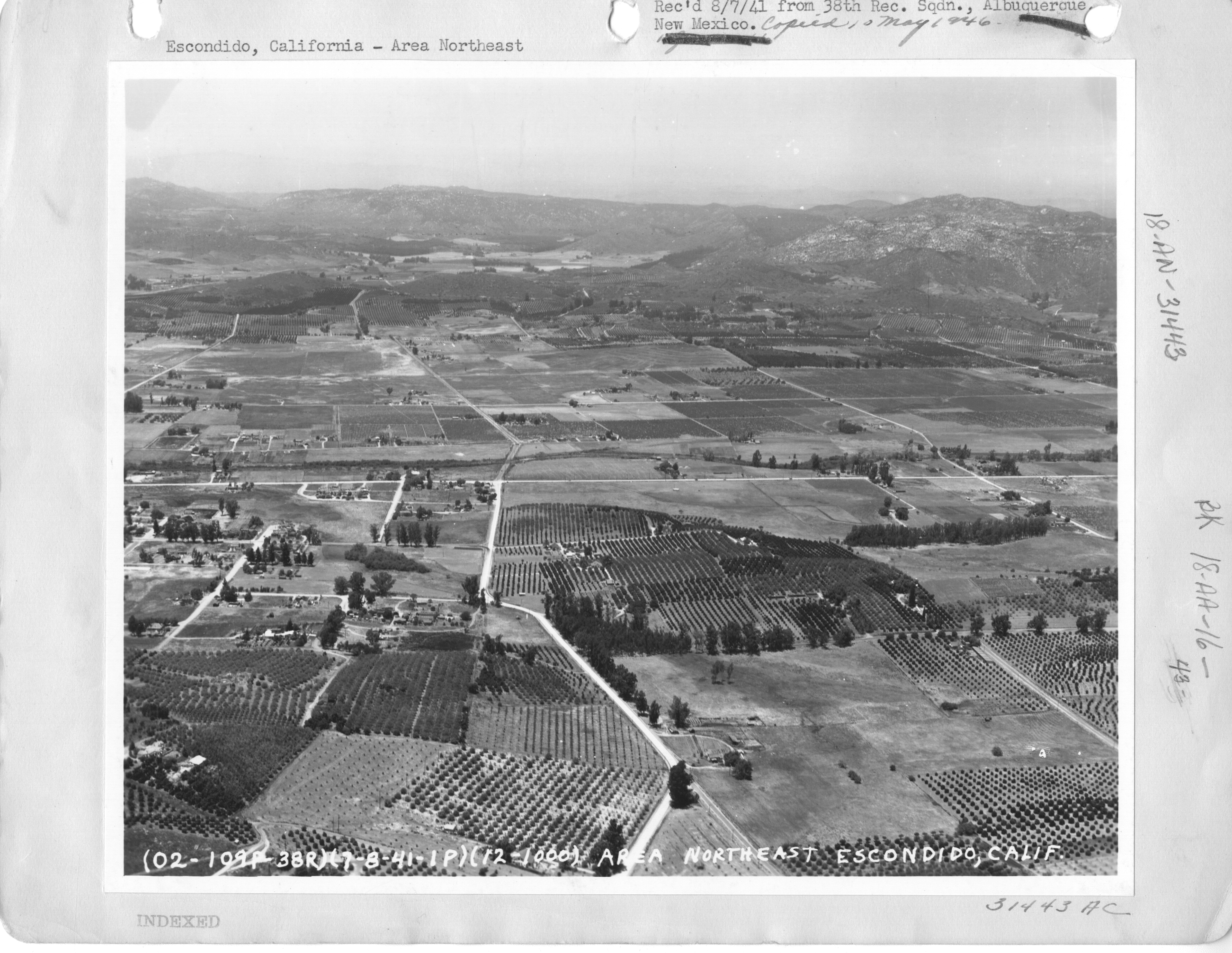 Black-and-white aerial view of gridded roads, orchards, farm plots, homes, and rocky hills northeast of Escondido.