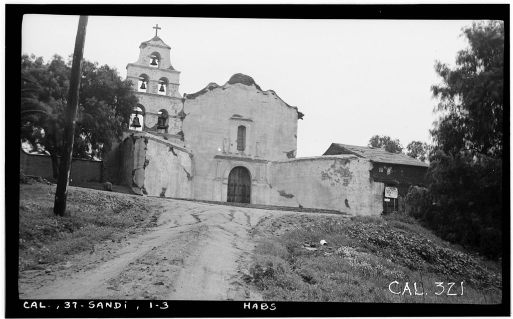 Black-and-white 1936 photograph of Mission San Diego de Alcalá’s weathered south façade and bell tower beside an unpaved approach.